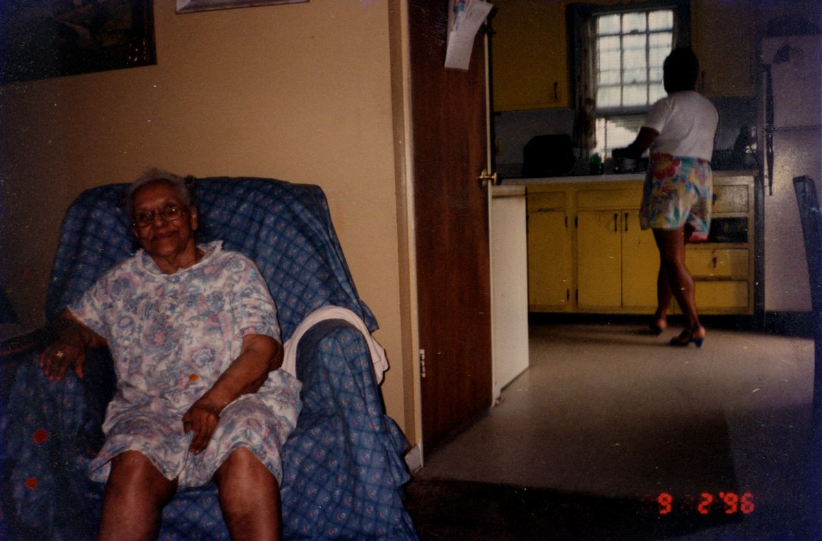 1996 - Gladys, aged 90, sitting in couch and Shirley (?) in the kitchen in the back.